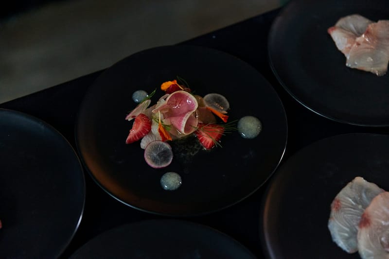 Plated hamachi crudo with strawberries and radish slices on black plates, seen from above