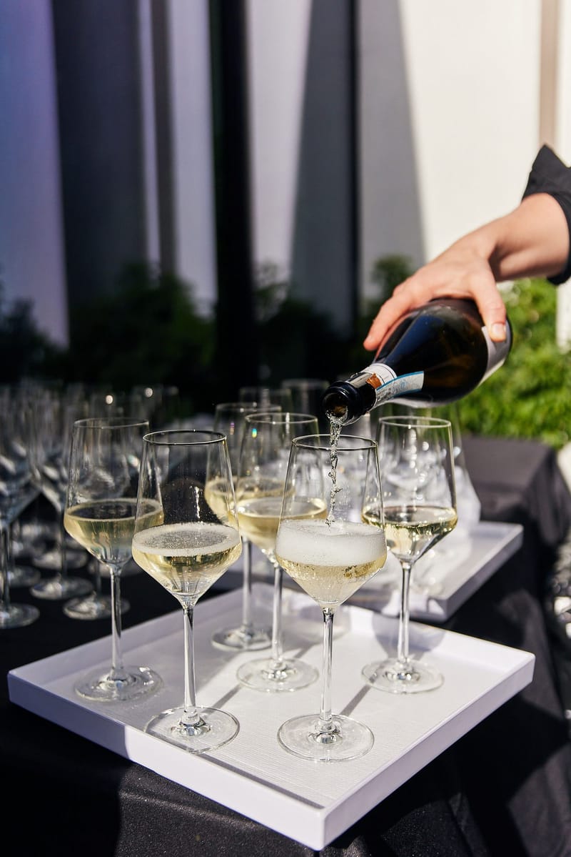 White wine being poured into glasses lined up on a white tray