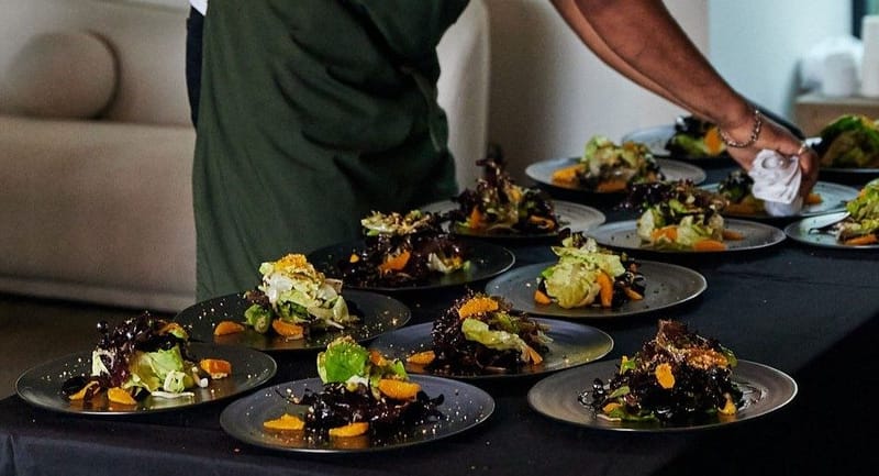A server garnishing rows of plated salads before they go out
