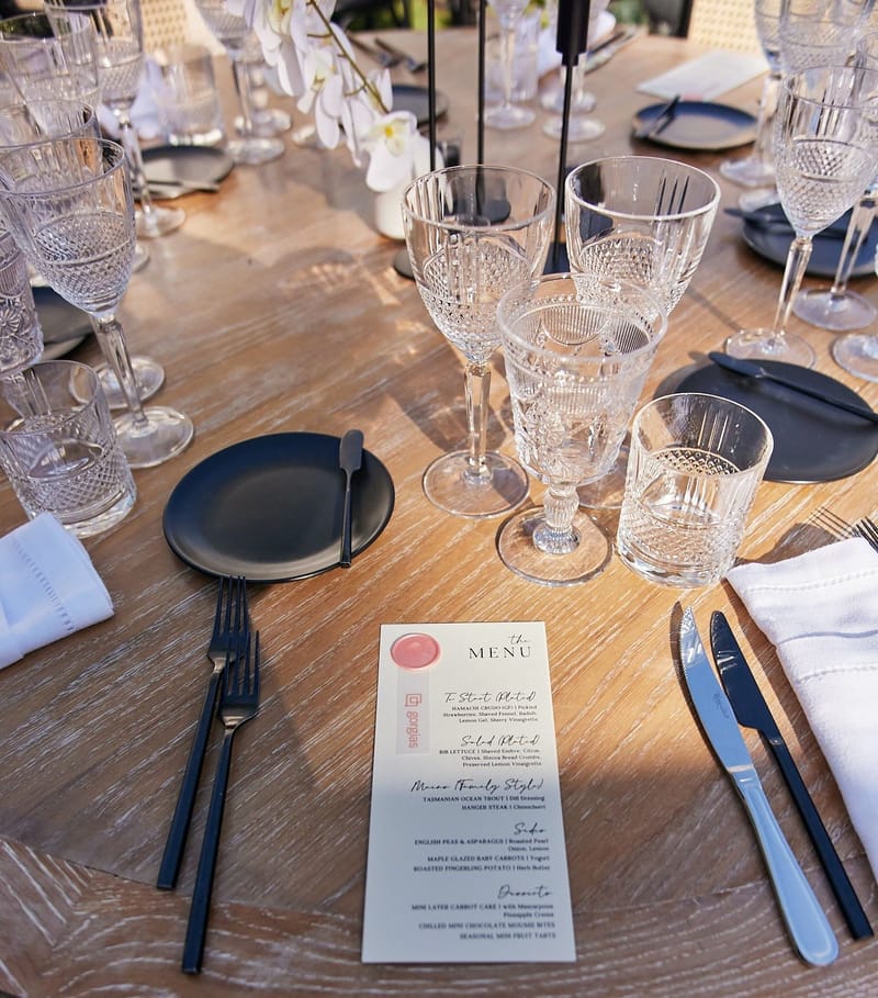 Place setting with crystal glasses, a black plate and a Gorgias menu card with a pink wax seal