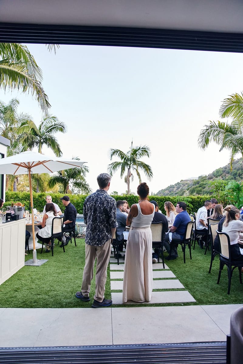 Two guests on stepping stones looking toward dinner tables on the lawn under a white umbrella