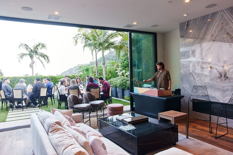 A DJ playing in a living room with Gorgias pillows while guests dine on the lawn outside