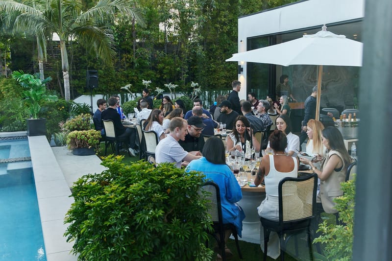 Guests dining at round tables beside the pool under a white umbrella