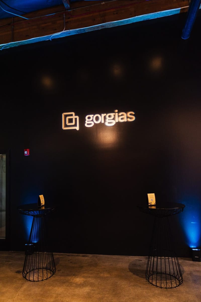 Illuminated Gorgias logo on a dark wall with two high-top tables