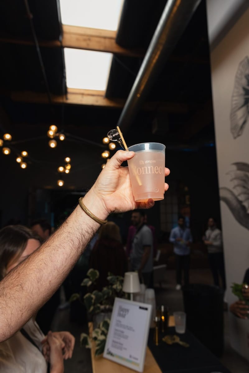A guest holding up a pale cocktail in a Gorgias Connect cup under string lights