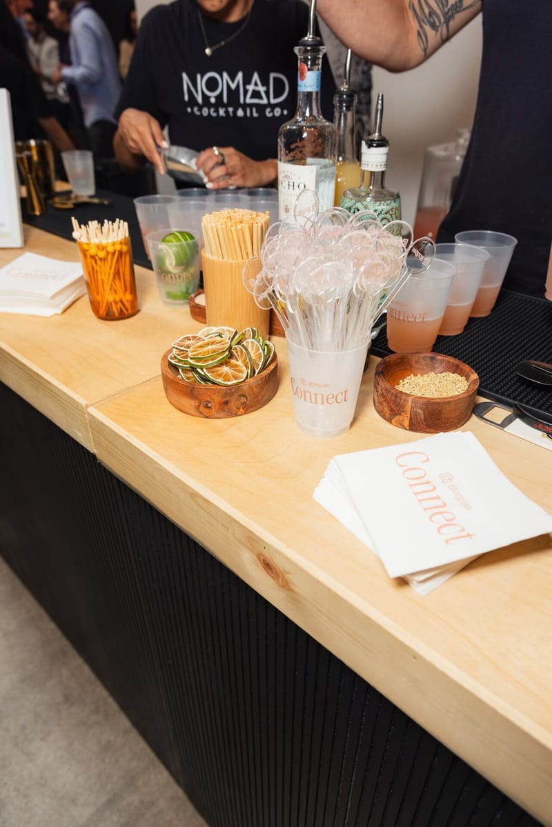 A NOMAD Cocktail Co bartender working a bar counter laid with bottles, dried citrus, stirrers and napkins printed Gorgias Connect