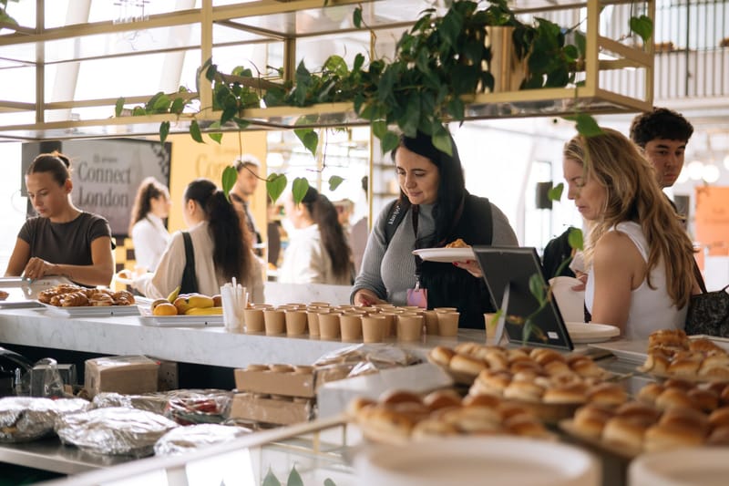 Guests helping themselves to pastries and lunch at a long counter under hanging plants