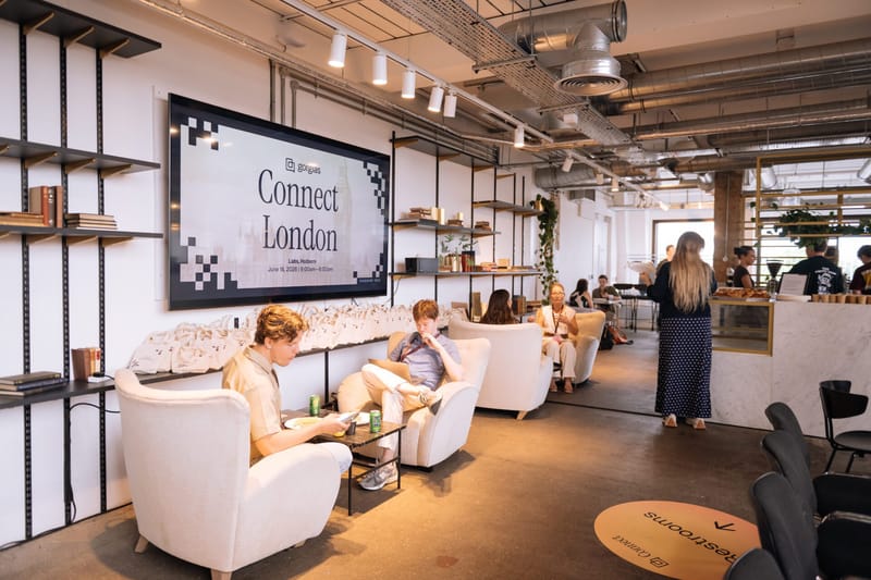 Guests relaxing in white armchairs below the Gorgias Connect London screen and the tote bag shelf