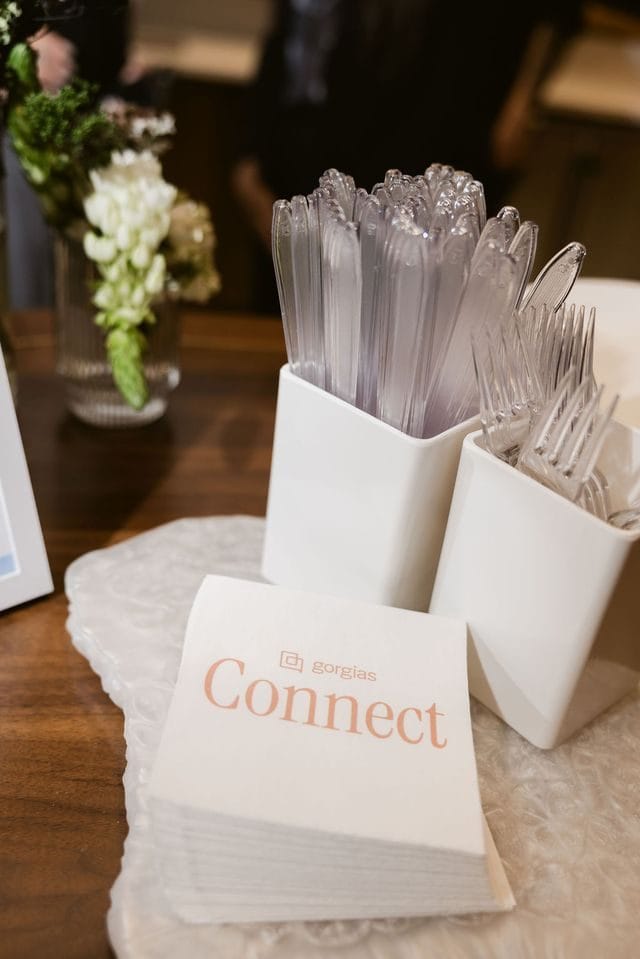 Napkins printed with Gorgias Connect beside cups of cutlery and white flowers