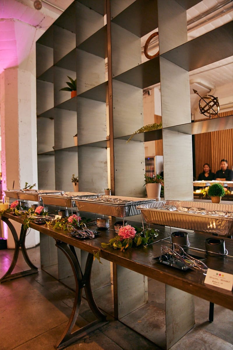 Buffet line of silver chafing dishes set up beside tall metal shelving