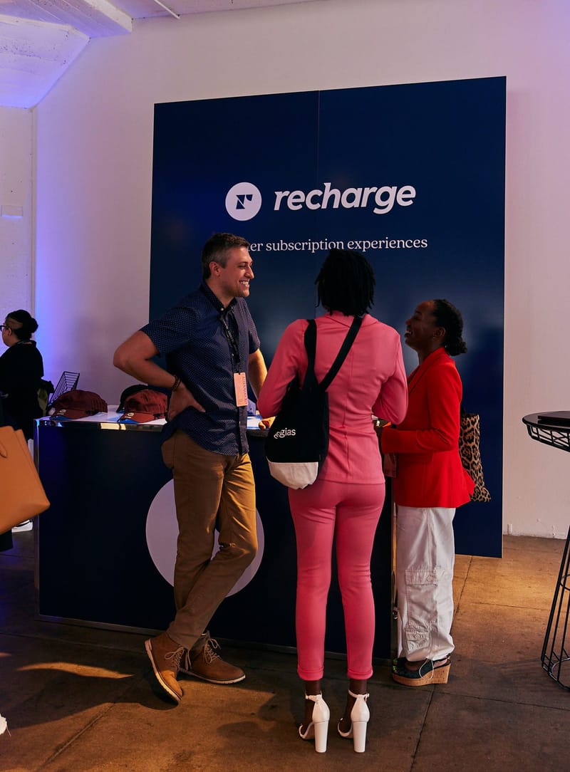 Guests talking in front of a navy Recharge sponsor space