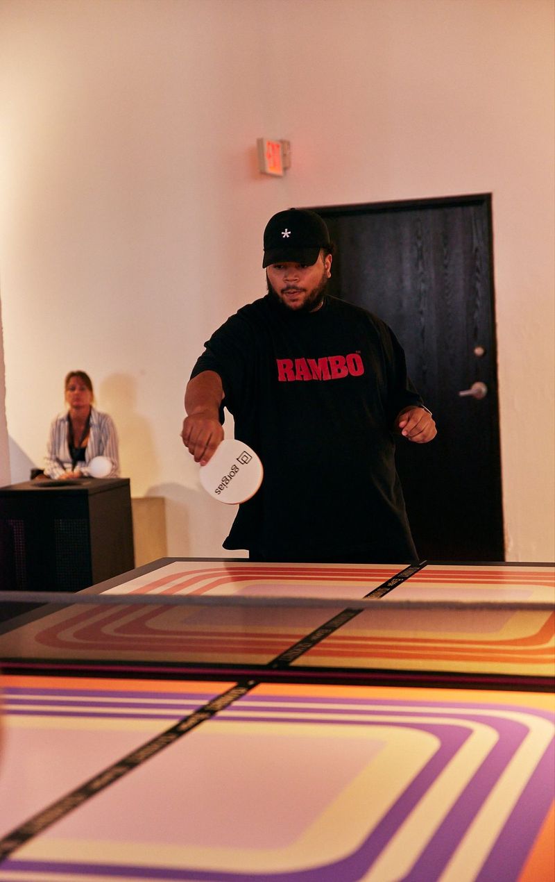 A guest in a black cap playing ping pong on a striped retro table with a Gorgias paddle