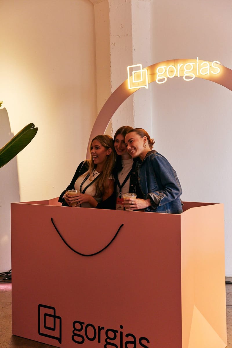 Three guests posing inside a giant pink shopping bag printed with Gorgias, under a neon Gorgias arch