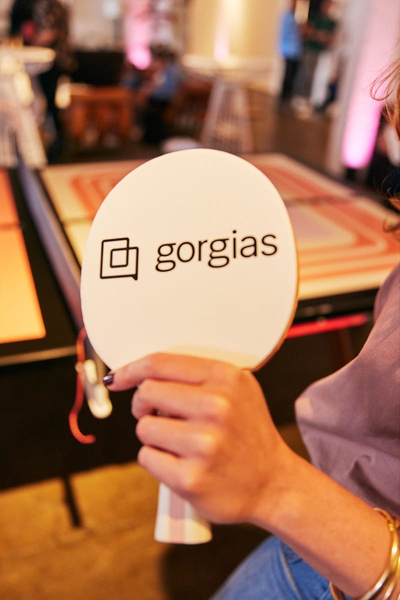 Hand holding a white Gorgias paddle over a ping pong table