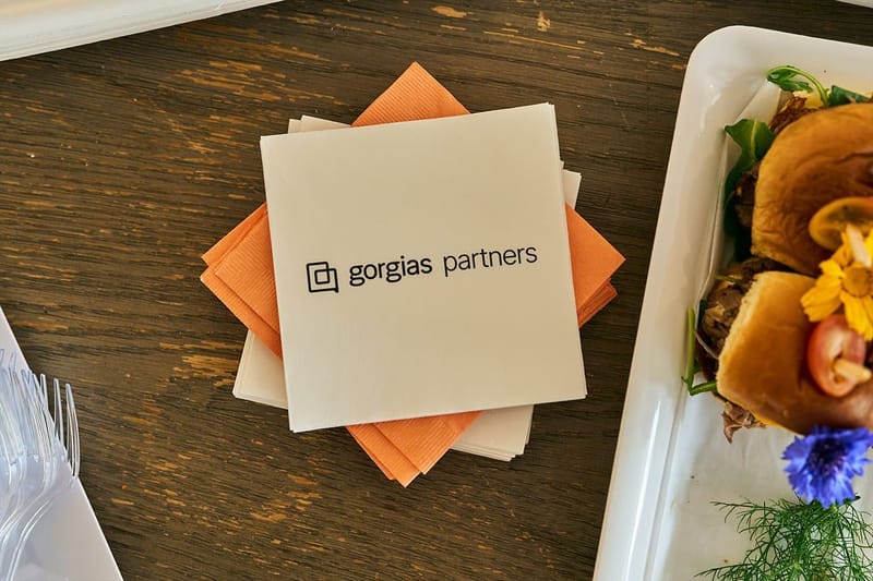 A cream napkin printed gorgias partners on orange napkins, beside sliders topped with edible flowers