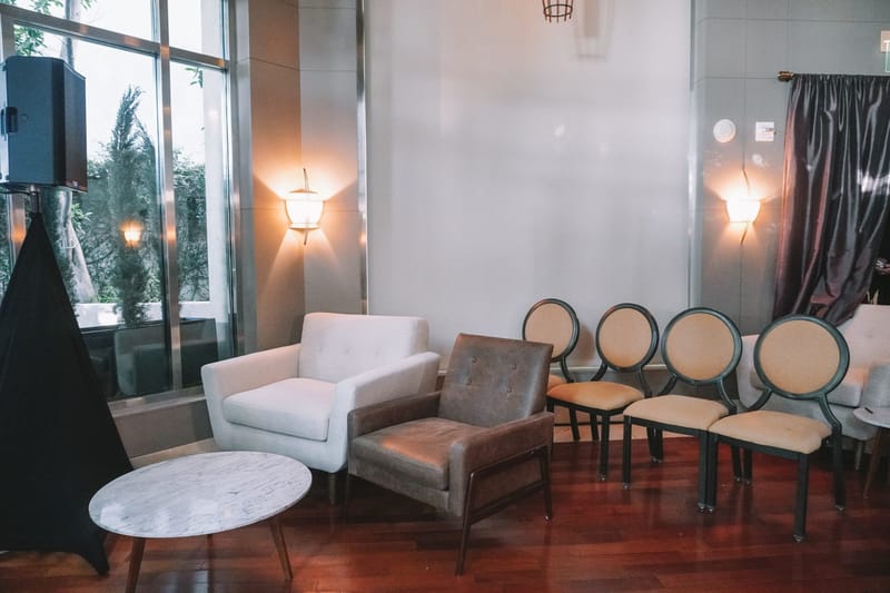 Lounge corner with a white armchair, a leather armchair, a marble side table and round-backed chairs by tall windows