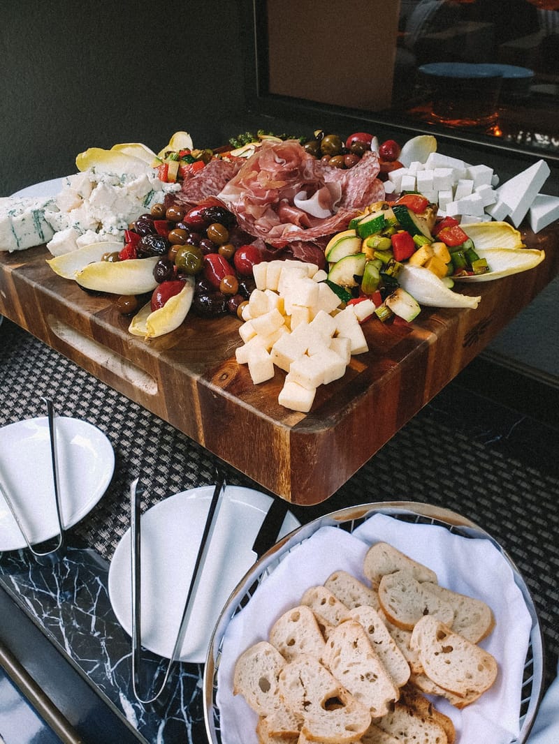 Charcuterie board of cured meats, cheese cubes, olives and vegetables beside a basket of sliced bread