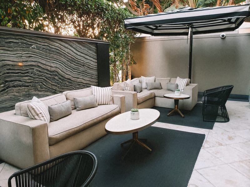 Outdoor patio lounge with cushioned sofas, an oval coffee table and a large umbrella against a stone wall