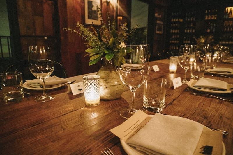 Candlelit place setting with a folded napkin, a printed menu card, glassware and small place cards