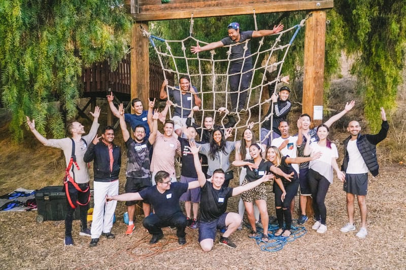 Group of guests with raised arms posing on and in front of a rope net hung from a wooden frame