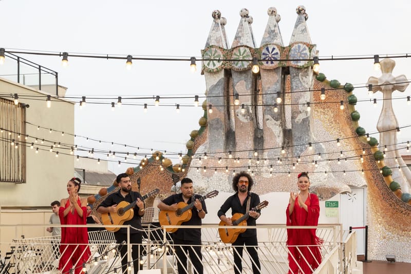 Three guitarists and two dancers in red dresses performing in front of mosaic chimneys