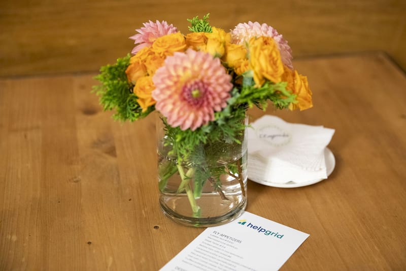 Dahlias in a glass vase beside a HelpGrid appetizer menu card