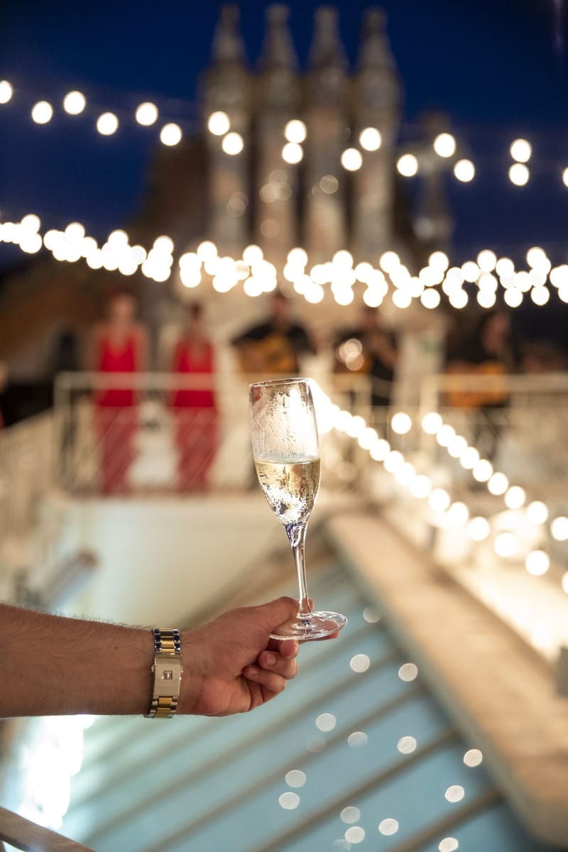 A hand holding a glass of champagne under string lights with blurred dancers behind