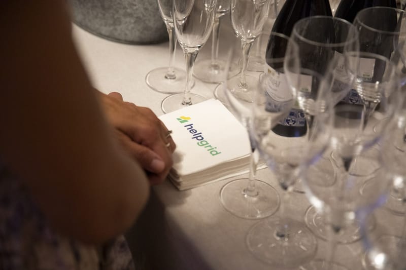 Hand resting on a stack of HelpGrid napkins beside champagne glasses