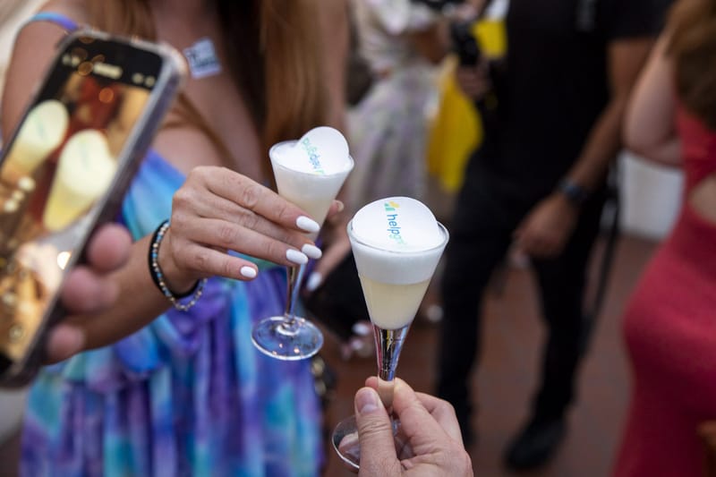 Guests clinking foam-topped HelpGrid cocktails while one films on a phone