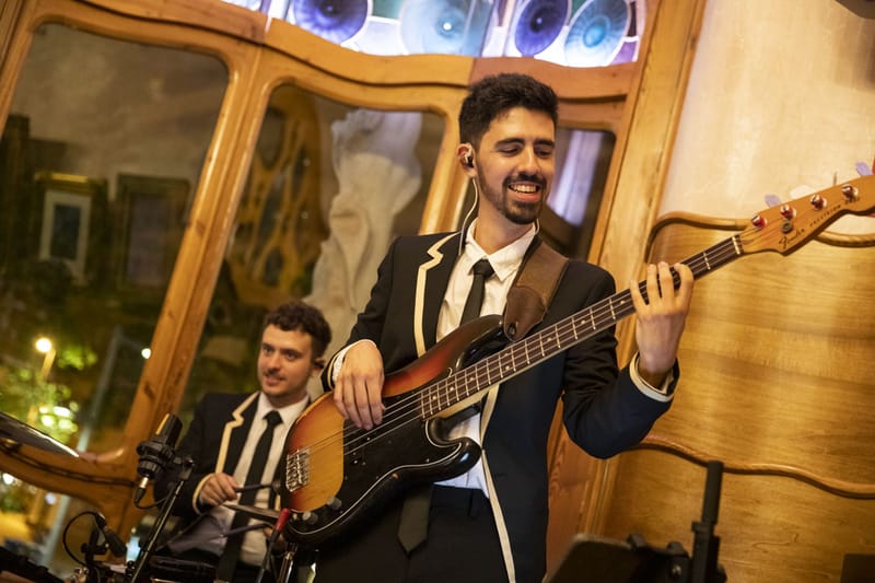 Bass player in a suit smiling beside a drummer, stained glass above them