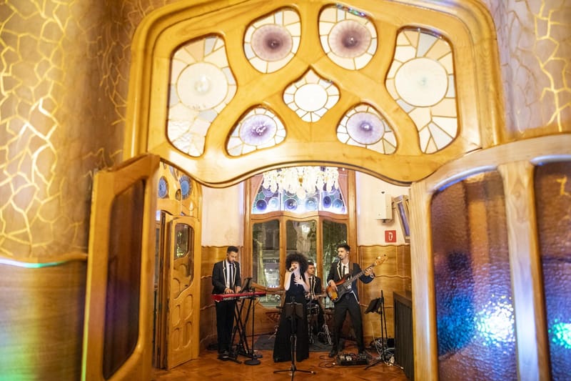 Band with a singer, keyboard, drums and bass in a gold room under an ornate stained glass window