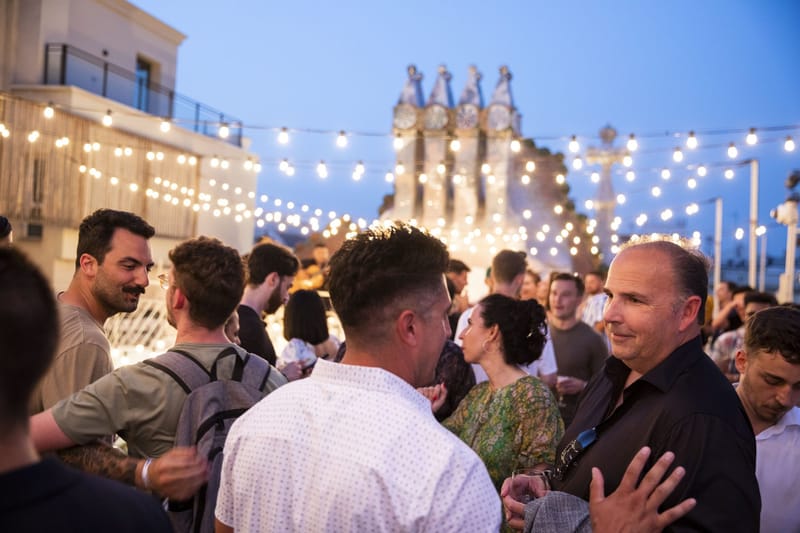 Guests talking on the roof terrace at dusk under string lights with mosaic chimneys behind