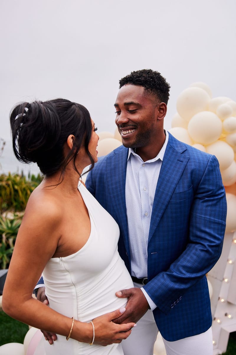 Expecting mother in a white halter dress smiling with a man in a blue blazer