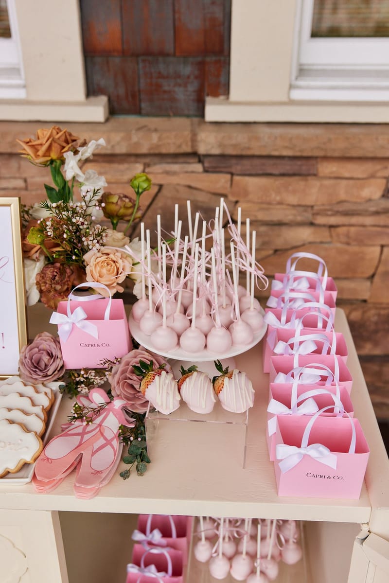 Pink cake pops, white-drizzled strawberries, ballet slipper napkins and pink Capri & Co. gift bags with white bows