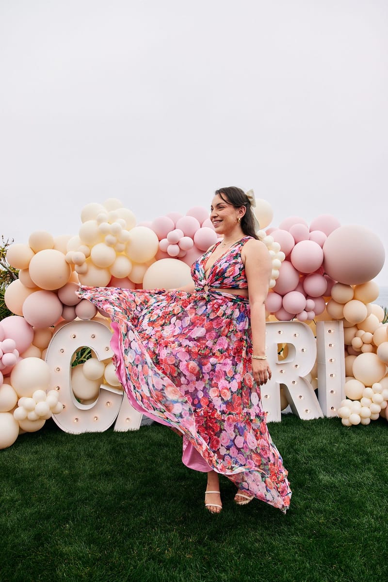 Guest in a pink floral dress twirling in front of the CAPRI light-up letters and balloons