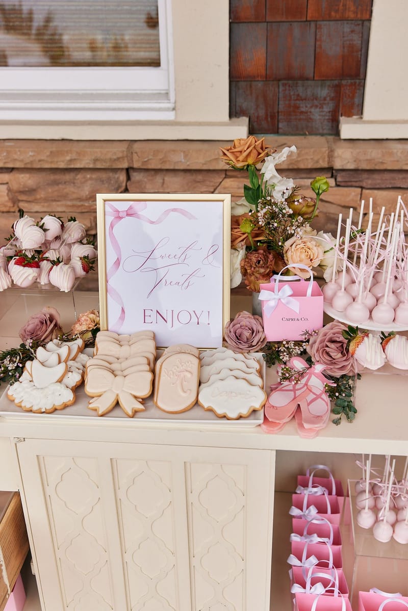 Sweets & Treats Enjoy! sign behind iced cookies reading Capri and baby, bow cookies and cake pops