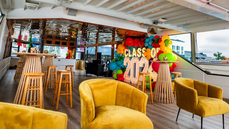 Mustard velvet armchairs and wooden high-top tables with stools, marquee letters and balloons in the background