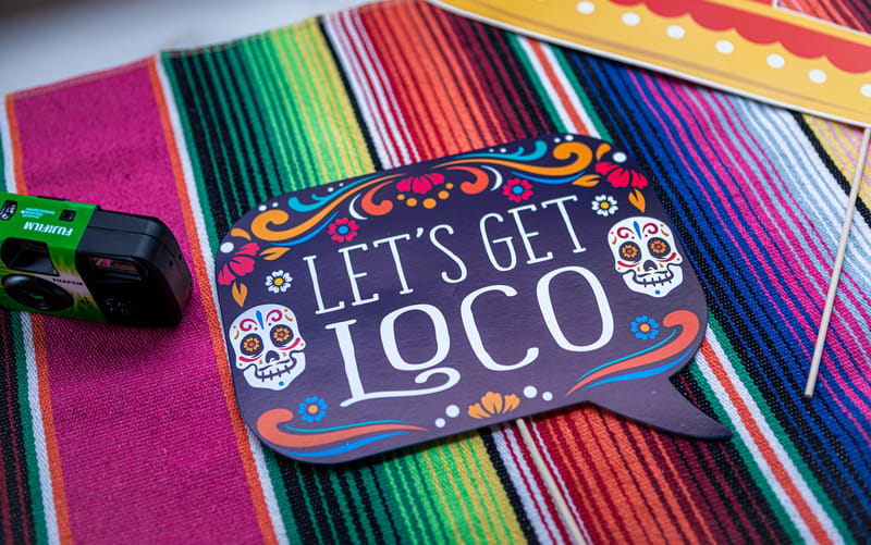 Let's Get Loco sugar skull photo prop and a disposable camera on a colorful serape runner