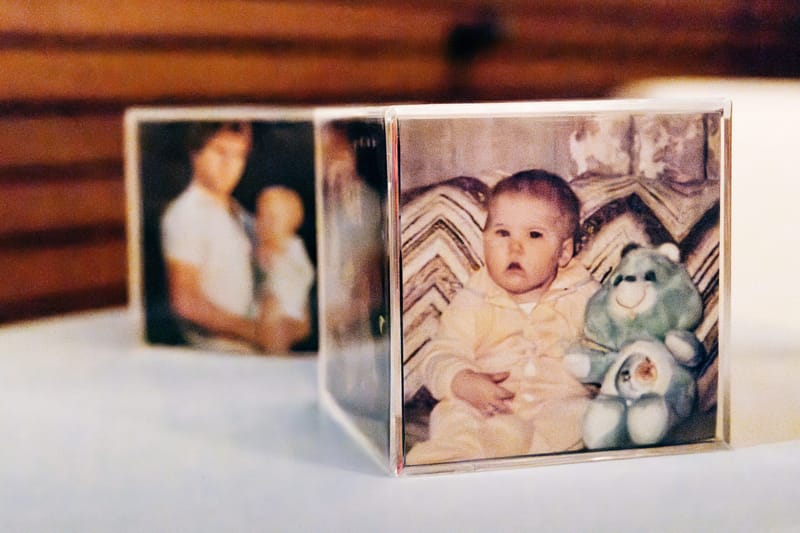Clear photo cube holding old family snapshots, including a baby beside a teddy bear