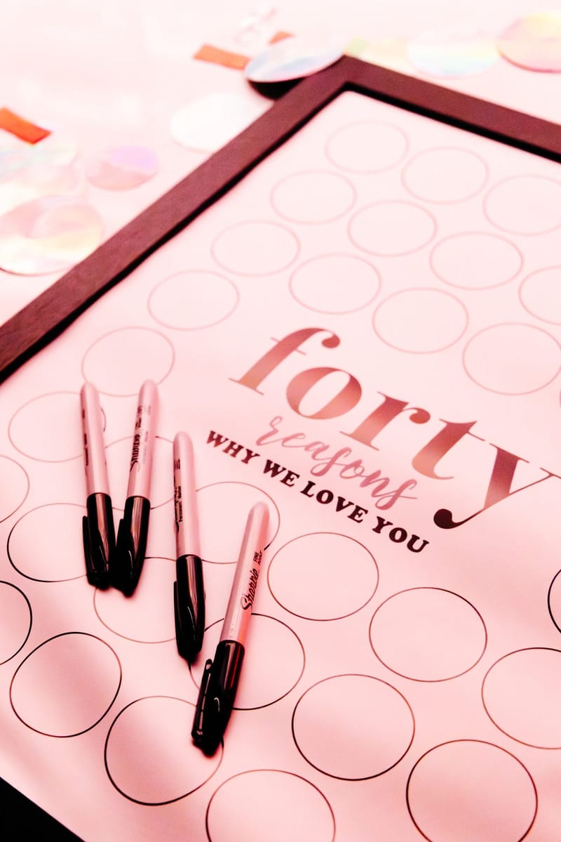 Pink board titled forty reasons why we love you with blank circles and black markers