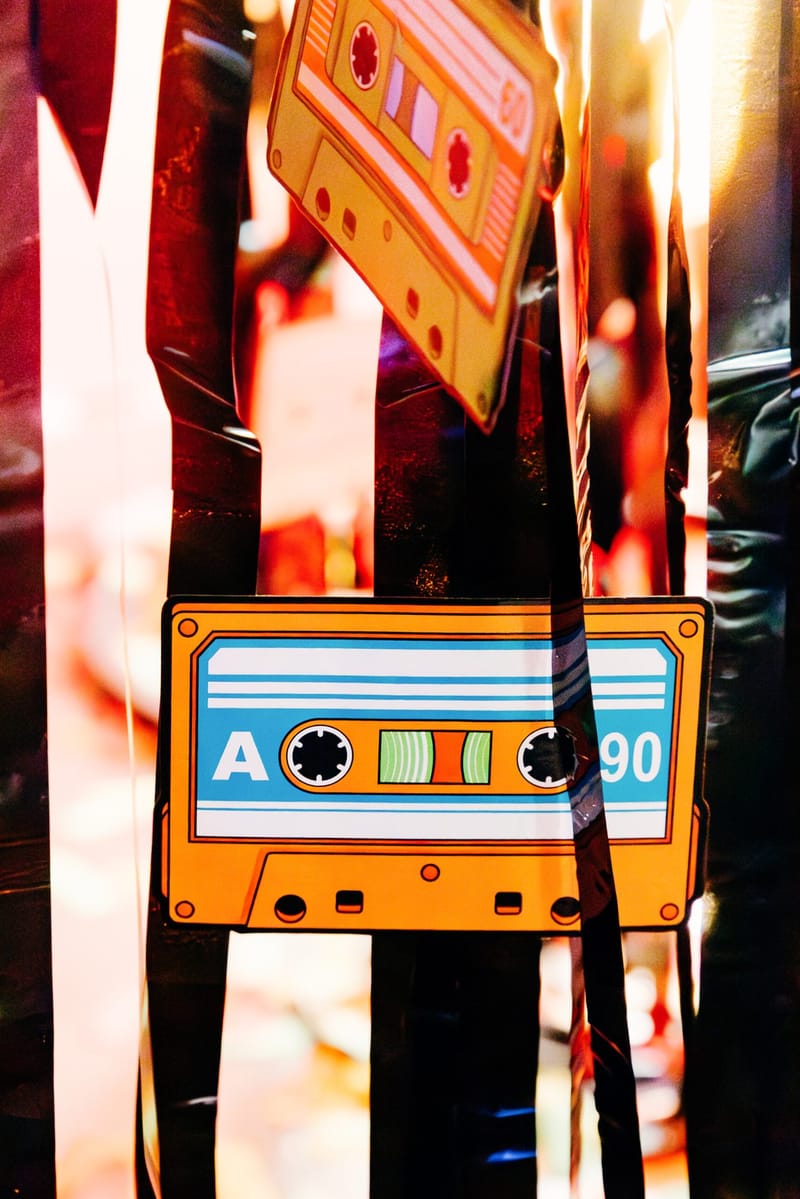 Orange and blue cassette tape cutout marked A and 90 hanging among black streamers