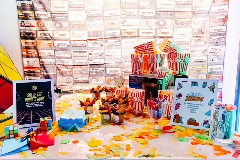 Snack table with popcorn boxes and Kristin's Kiddie Korner menu in front of a wall of cassette tapes