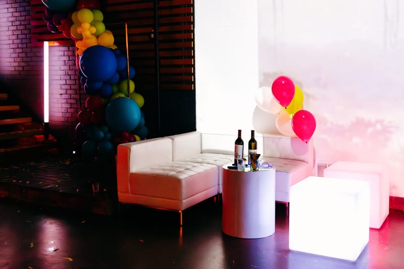 White lounge sofa with a glowing cube, wine bottles on a side table and balloons behind