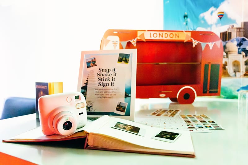 Snap it Shake it Stick it Sign it guestbook with a pink instant camera, a passport and flag stickers