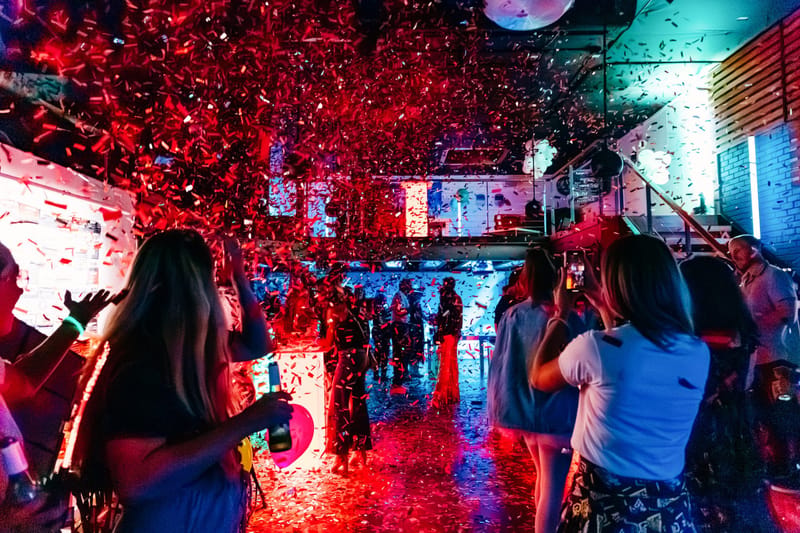 Red confetti raining over guests dancing in a colorfully lit room