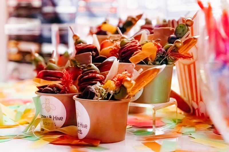 Cups of skewered charcuterie with fruit and cheese on a table scattered with confetti