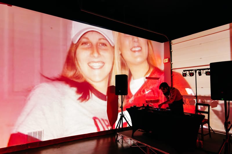 Old photo of two smiling young women projected on a wall above a DJ at the decks