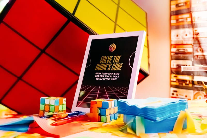 Solve the Rubik's Cube sign offering a bottle of fine wine, with Rubik's Cubes and a giant cube prop