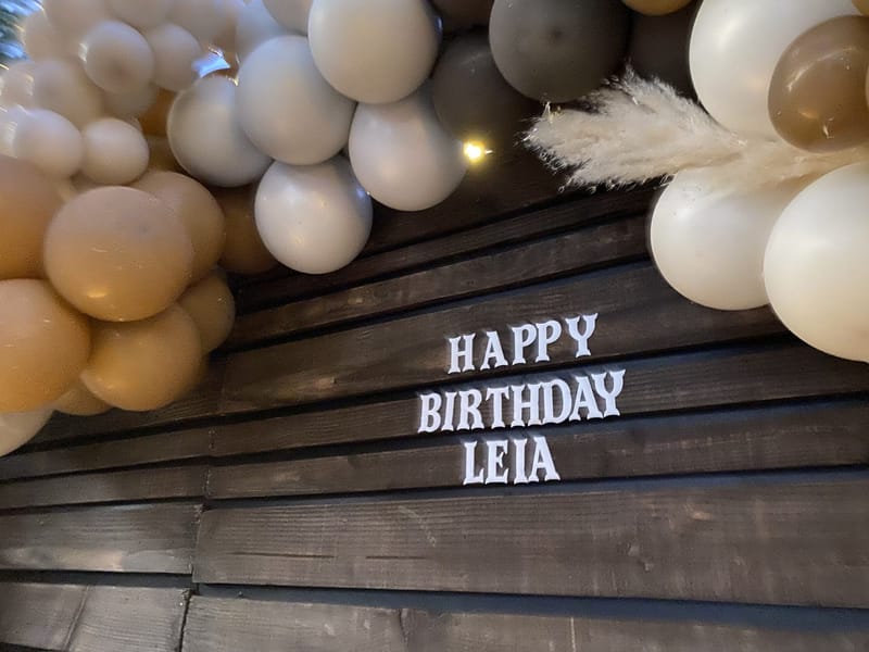 White HAPPY BIRTHDAY LEIA letters on dark wood planks under cream and tan balloons with pampas grass