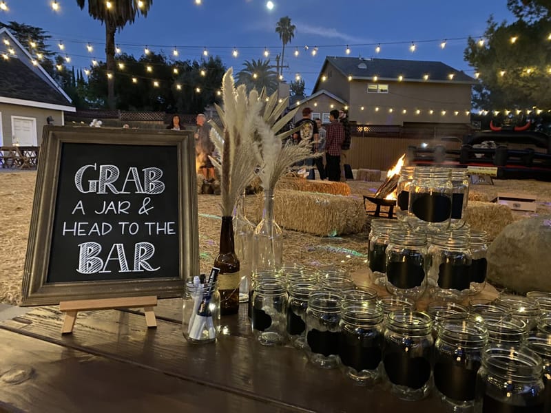 Chalkboard sign reading Grab a Jar & Head to the Bar beside rows of mason jars and pampas grass